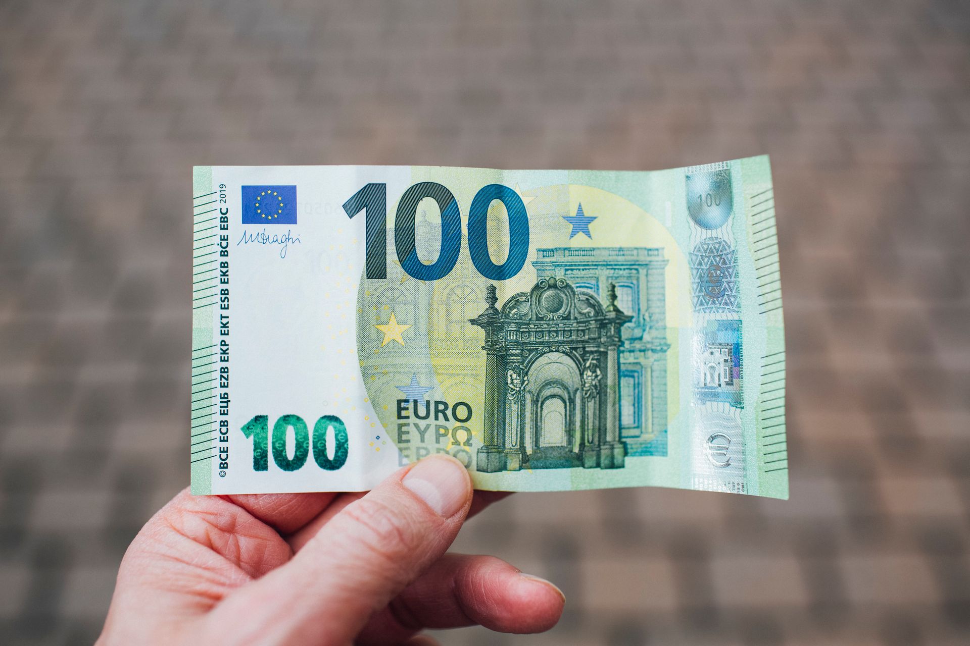 Personne tenant un billet de 100 euros devant un fond flou